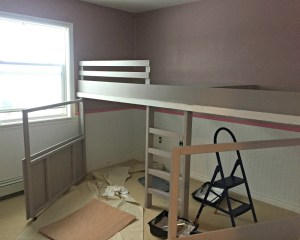 Instead of having the doors be solid plywood and then cutting out windows, it was going to be far cheaper to make half-doors out of half-sheets of plywood and leave the top of the doors open — framed with 2x2s. We put casters on the bottom of the doors so they’d slide more easily and not put too much weight on the hinges. We designed the swinging doors to be exactly the same size, to make things easier, and left enough room in the centre for the ladder. Typically, a bunk bed ladder leans out into the room so you can climb on a comfortable angle. But our kids have been climbers since they were babies so we knew we wanted to build a somewhat challenging ladder: straight up and down. (The bonus was that it wouldn’t take up any more floor space, because the bed was looking more and more gargantuan as we worked.) The final step of construction was adding a simple safety rail near the top of the mattress so our daughter wouldn’t tumble out of bed at night — it would be a seriously long, hard fall. We kept the bottom of the bed open, since that’s where it met with the ladder, and decided not to put a rail around the play area. Since there’s no mattress there, the kids have somewhat of a natural ledge to keep them in. While the construction was pretty easy, it was priming and painting that monster that took most of the effort. As much as I really, really didn’t want to have to prime it, the associate at Kent gently convinced me that it was the best way to make sure the paint wouldn’t chip or flake. And so I primed . . . and primed . . . and primed. We chose a soft grey for the bed colour (PPG’s Rice Chips) to go with the new blush-coloured walls (PPG’s Pinot Noir), and we used SICO Furniture & Cabinet paint to ensure we’d get a durable finish. For a finishing touch, I nailed some thick trim on the doors and painted some of the trimwork a glossy un-tinted white. I traced a small dessert plate again and again on a sheet of MDF and my husband cut them out with his scroll saw to create the cutest scallop detail. I also added a shiny white metal mailbox, a vintage lock plate from Phillips & Chestnut Victorian Salvage and Decor, and house numbers sprayed gold inside a white oval frame. I hung cafe curtain rods inside each of the doors and used gold metal clips to hang homemade curtains in a beautiful deep rose. It really looks like a sweet little playhouse under there. For the elevated play area, I just covered the MDF ‘floor’ with some pink cotton fabric and stapled it tightly underneath — rather than painting the MDF and worrying about it getting scratched up underfoot. With a few throw pillows and rattan storage bins, it’s the perfect spot for our daughter’s Shopkins collection and other small toys. She loves playing up there, and the best part is that I don’t care how messy it gets because you can’t see it! Even though our daughter’s new loft bed is massive, it doesn’t feel like it takes up the entire room because it’s so multi-functional. The rest of her room is empty — except for the coral bookcase built from end tables that I showed you a few weeks ago — so there’s plenty of breathing room. What started off as an idea for a simple loft bed turned into something much more involved, but I’m so happy with how it turned out. By thinking vertically, we were able to double the available play-space while also hiding the toy clutter. I swear, her bedroom has NEVER stayed this clean — or looked this beautiful.